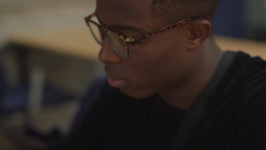 Black man wearing glasses looks down and think indoors during daylight