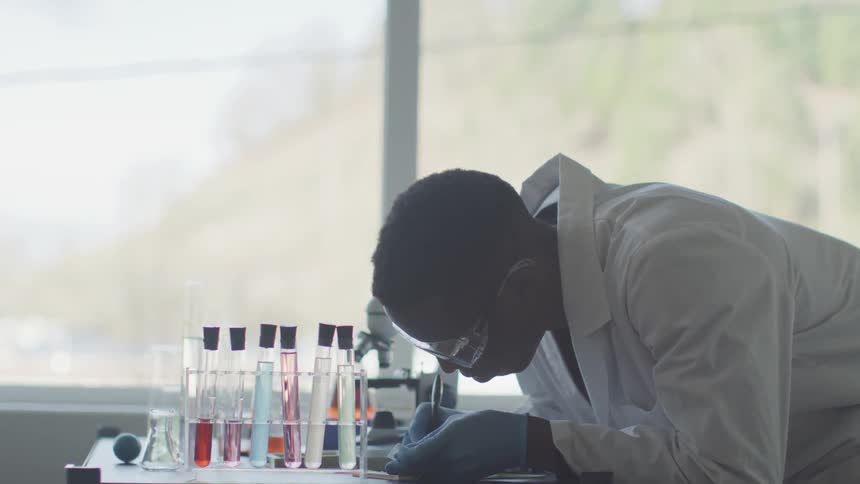 A man in a lab coat works near test tubes and a microscope