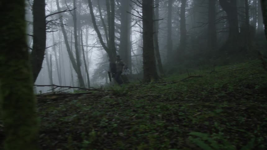 A man carrying a surfboard as he runs through the woods on a mystical and foggy day