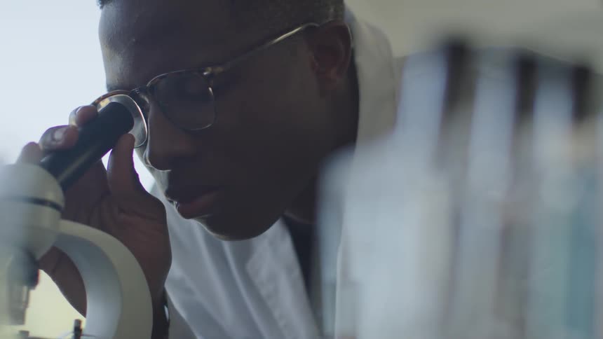 A man wearing a lab coat looks through a microscope in a laboratory