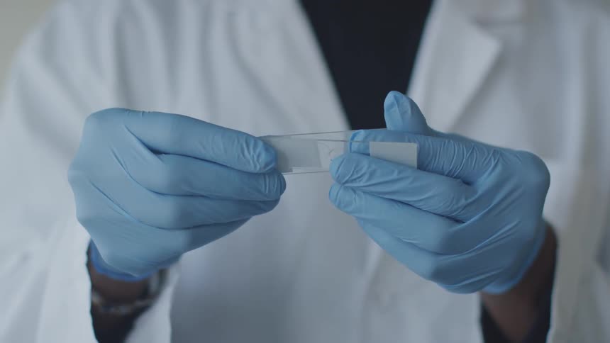 A lab worker examines two microscope slides