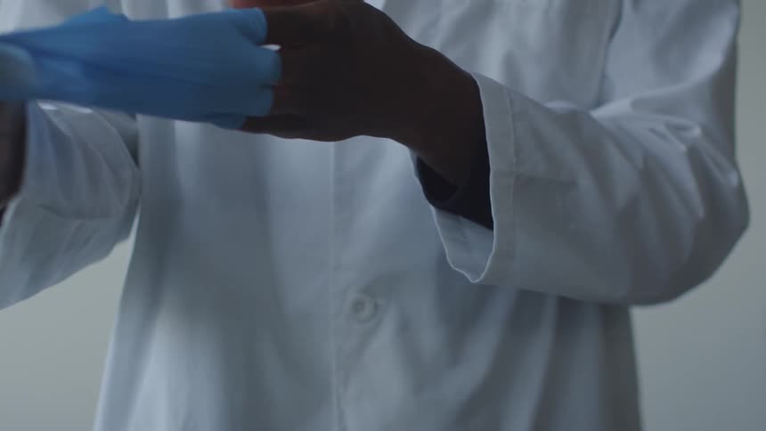 A person in a lab coat takes off blue latex gloves