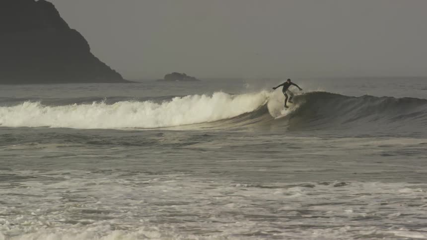 A man rides a wave surfing on a cloudy day along the Oregon coast in a solo session