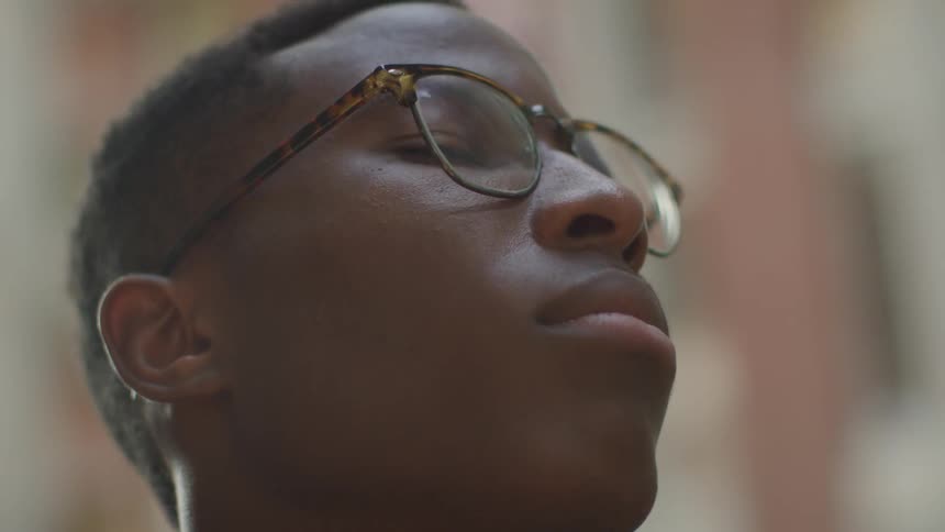 Black teenager who wearing glasses looks ahead indoors during daylight