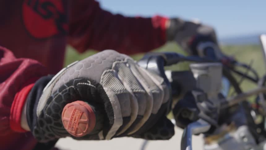A motorcyclist grips the handlebars of a motorcycle while wearing gloves