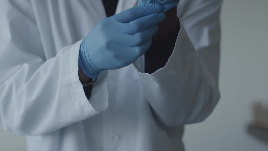 Person wearing a lab coat putting on rubber gloves