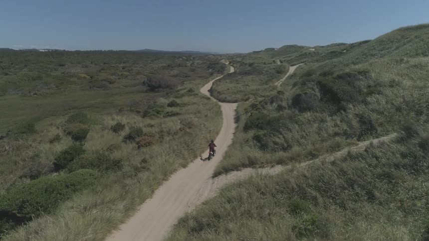 A person riding a motorbike through dirt paths in wide grassy plains