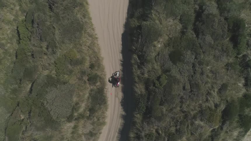 A dirt bike rides down a sandy trail