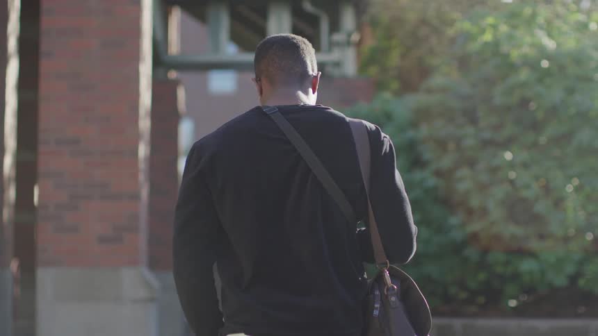 Man carrying a bag walks down the street towards a building