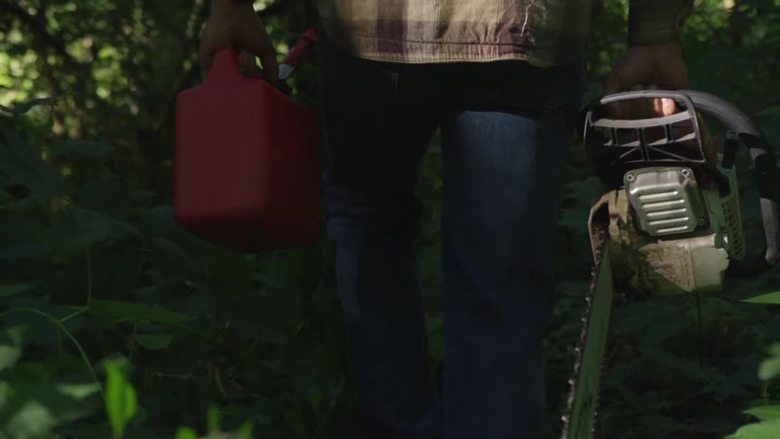Man carries a chainsaw and a gas can through the forest