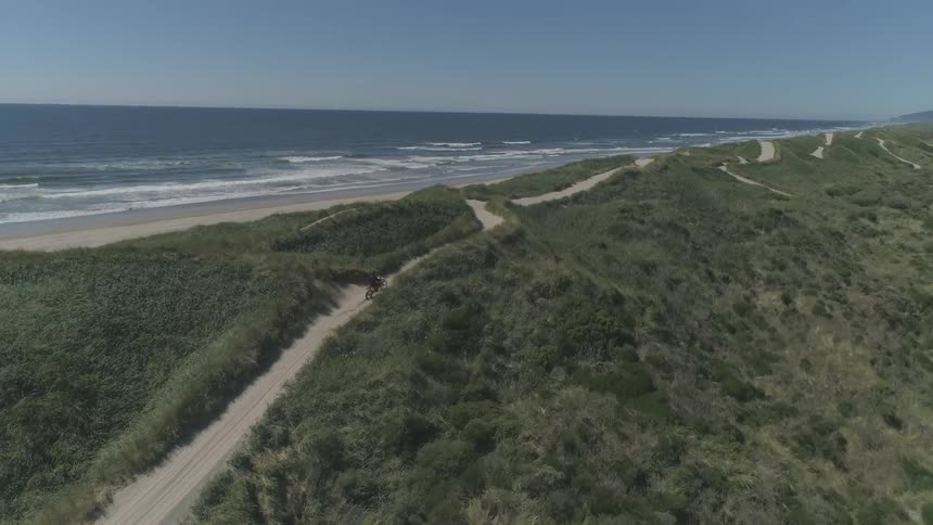 A person rides a dirt bike down a sandy trail next to the ocean