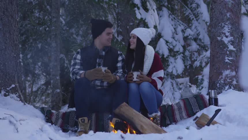 A young man and woman sitting before a campfire in a snowy landscape