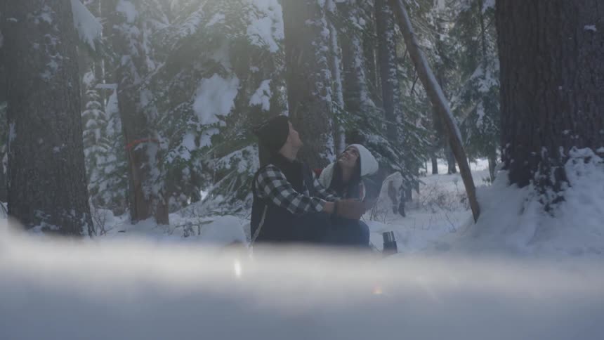 Couple looking up sitting in the in the snow surrounded by trees