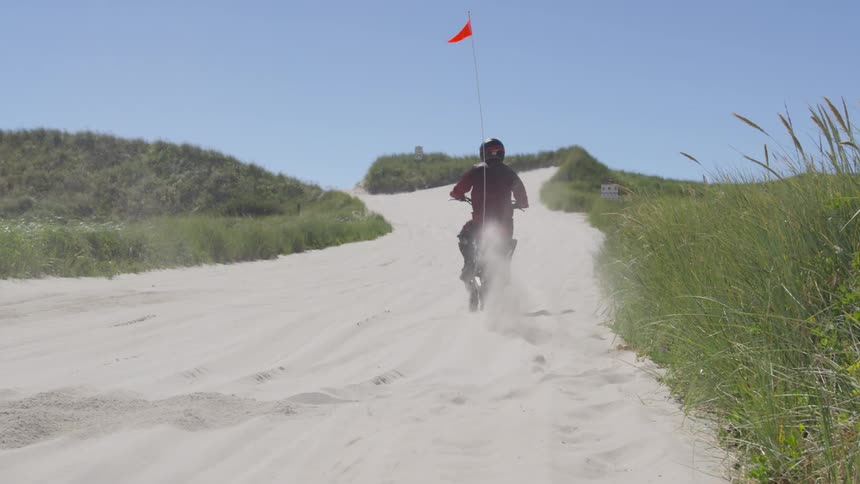 A person riding a dirt bike is kicking up sand while turning on his bike