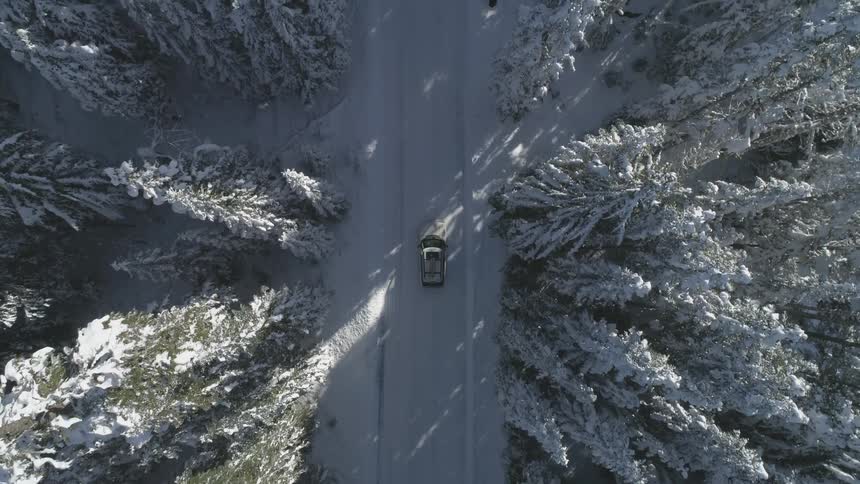 A car drives down a snowy road through the forest