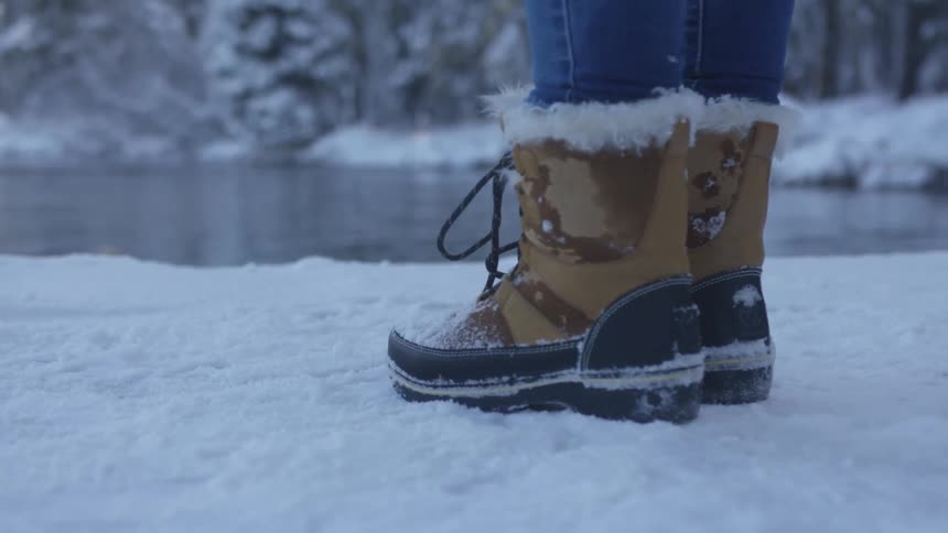 A person wearing boots stands on the shore of a lake in winter