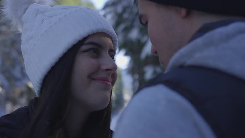 A couple looks into each other's eyes in snowy woods