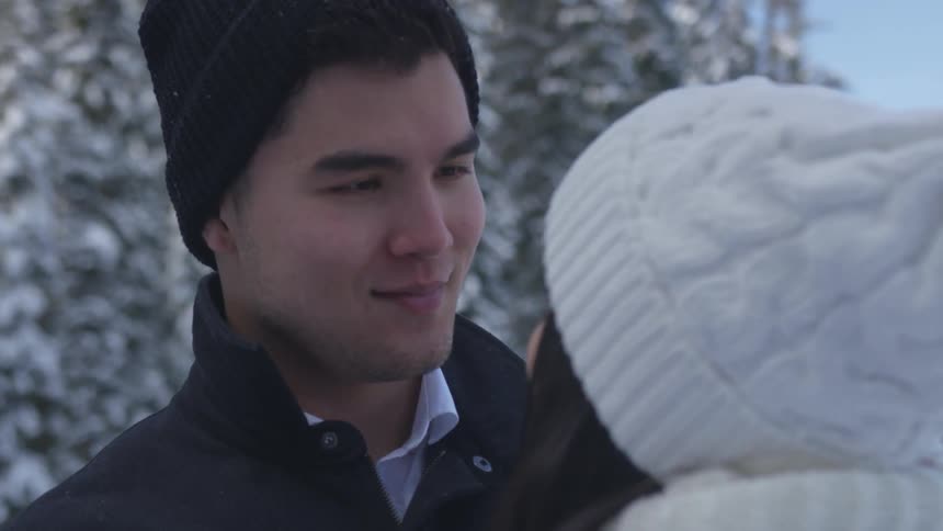 Man and woman wearing winter clothes glance each other romantically in the forest