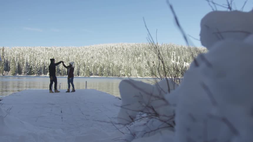 Two people dance in the snow by the lake