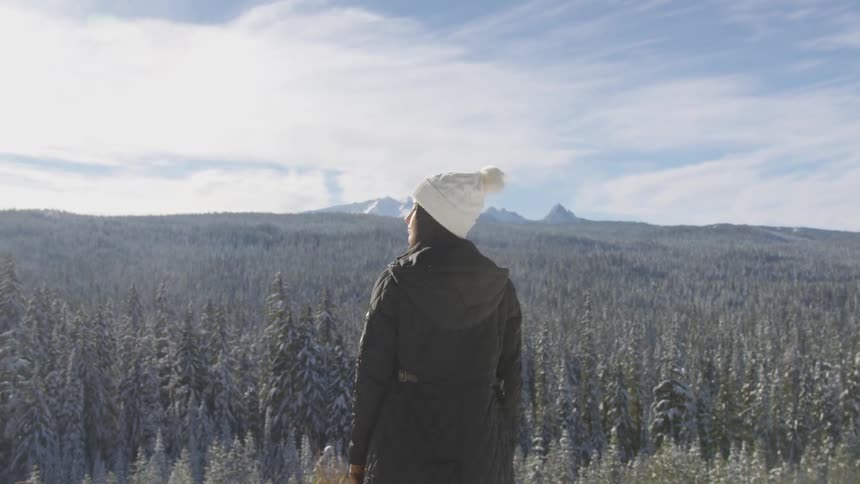 A woman in a winter hat and coat stands in a forest