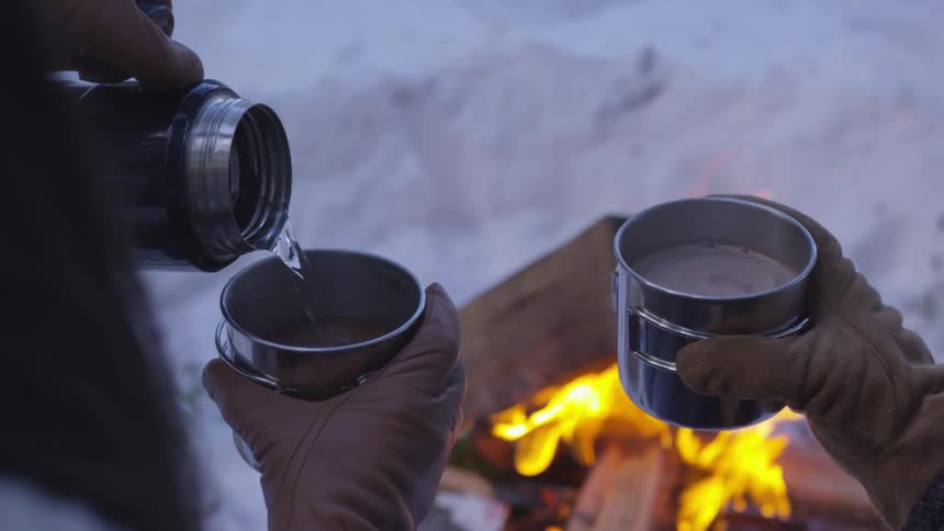 A person fills a metal cup from a thermos