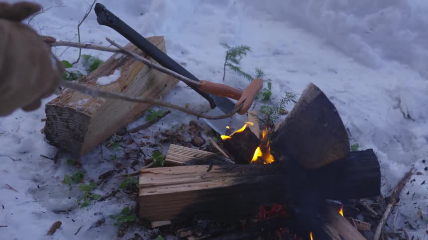 Two people hold hot dogs over an open flame