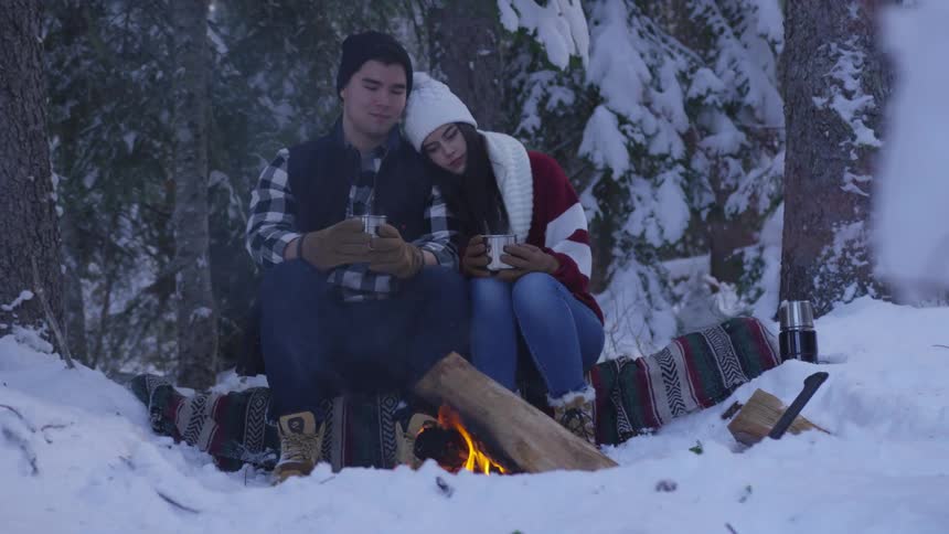 A woman and a man sit near an open fire