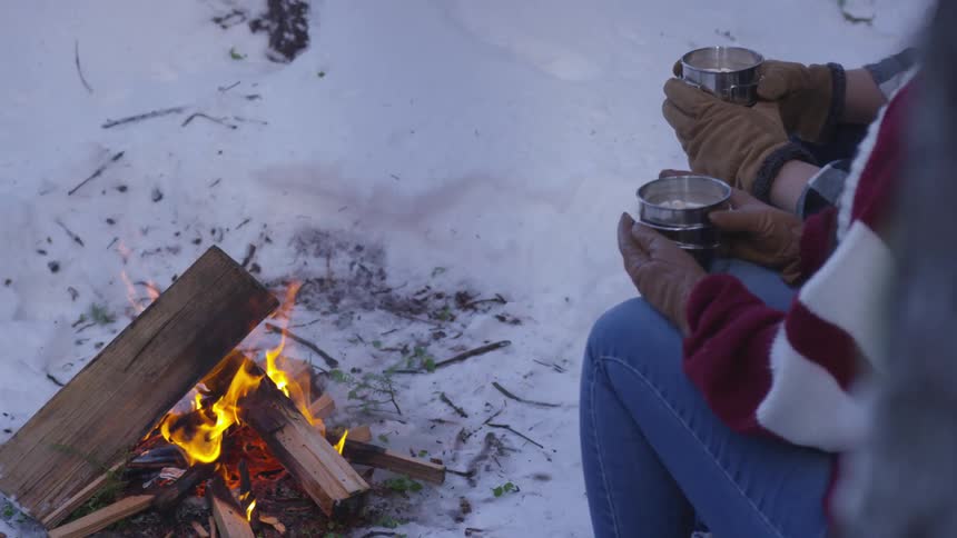 People sit around a fire holding cups