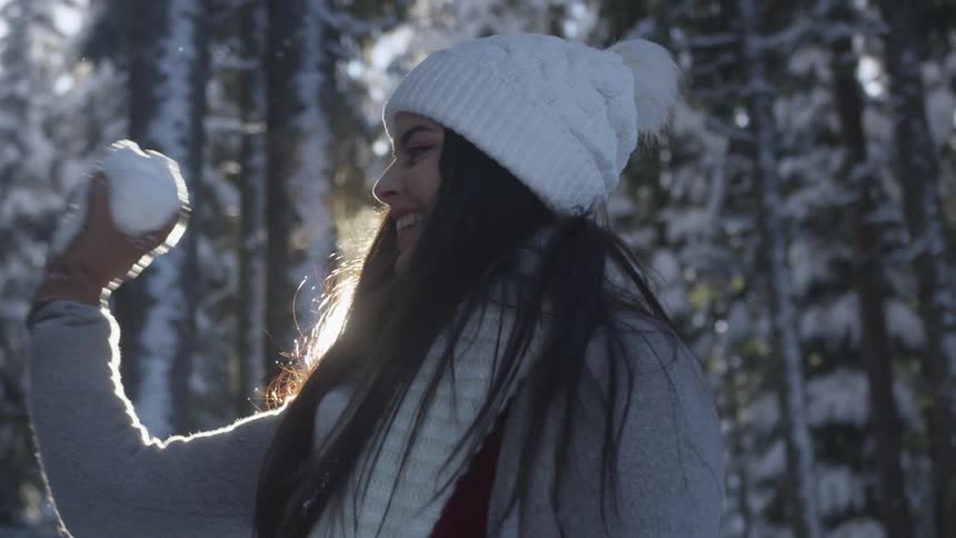 Young woman throws snowball in forest in winter