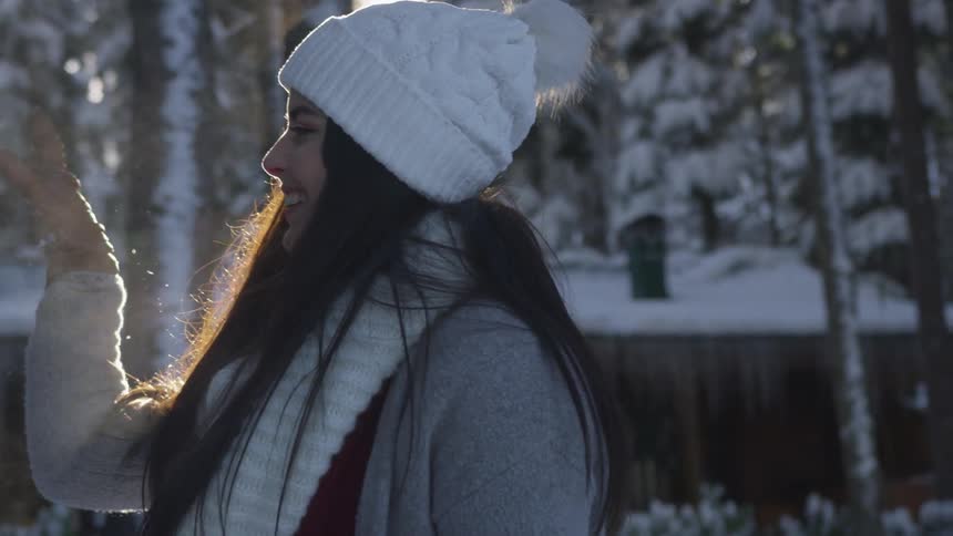 A woman laughs as she tosses a snowball with the sun shining through snow covered trees