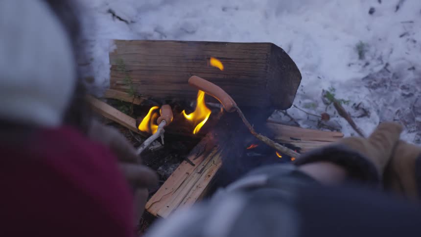 Two people roasting hot dogs over a fire