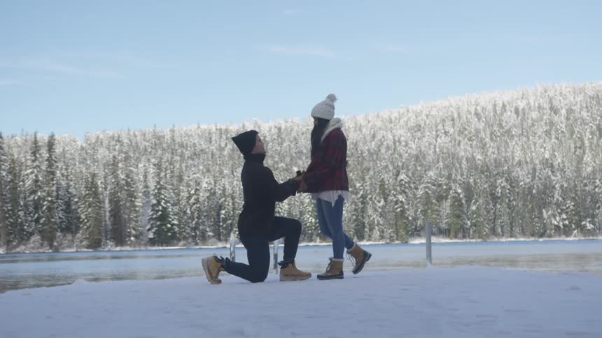 A man gets down on one knee and proposes to a woman while outside in the snow