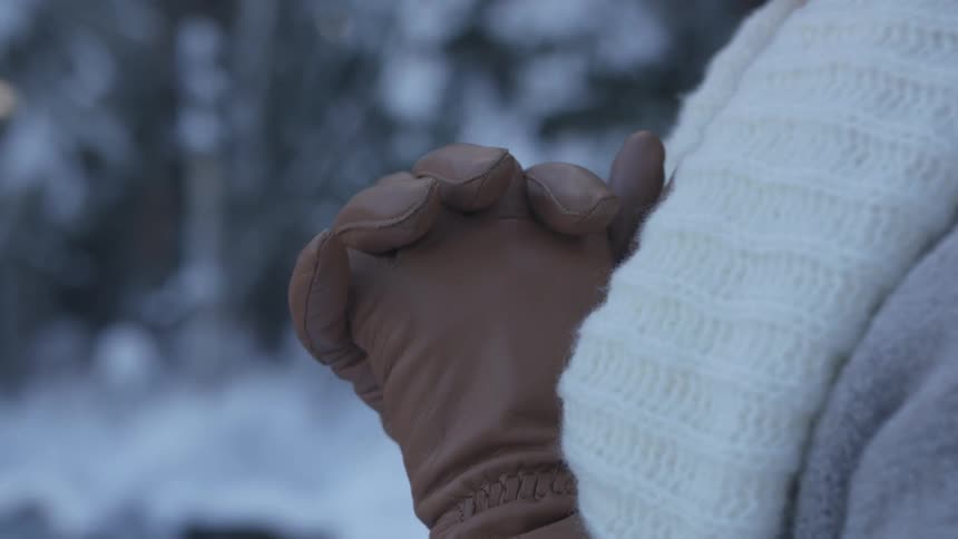 Woman wearing scarf and gloves folds hand and prays in the forest at dusk