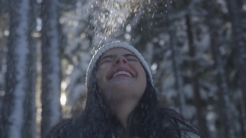 A woman throws a handful of snow into the air and laughs