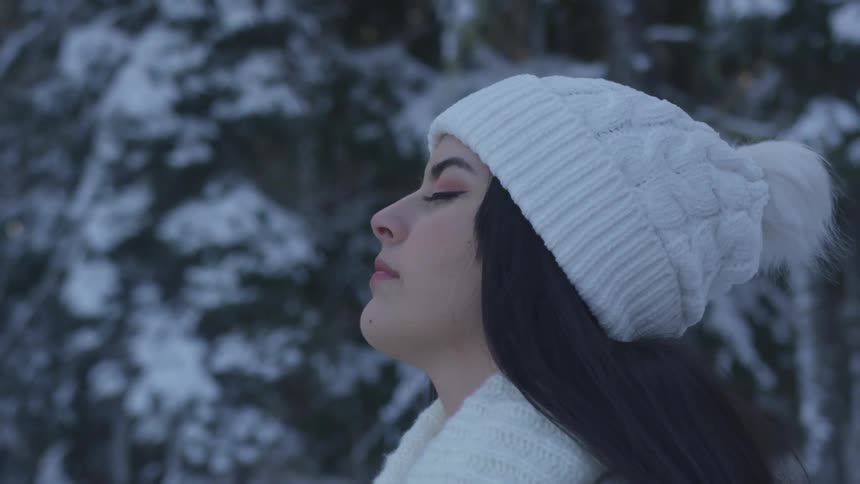 Woman stands in a snowy forest with her eyes closed