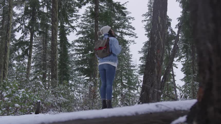 Woman stands on tree trunk and looks up in the snowy forest during daylight