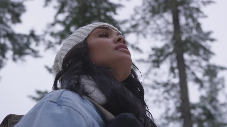 A lovely tan woman wearing a white winter cap tilts her head upwards while having her eyes closed