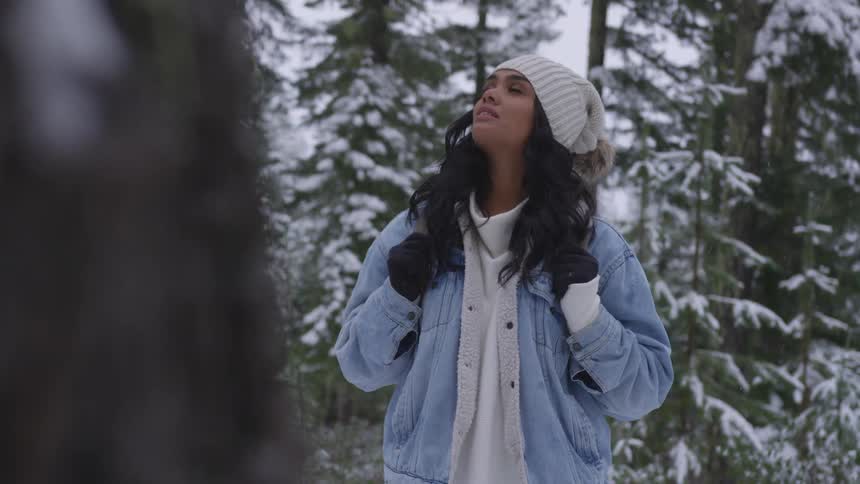 A woman stands in a snowy forest looking up