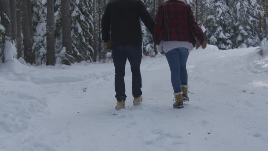 Man and woman walk on the snowy forest path during daylight