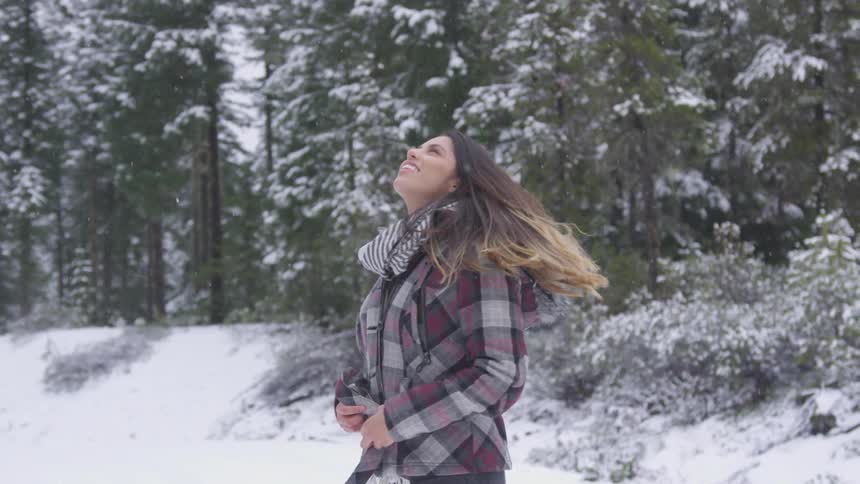 Woman walks down on the snowy forest path while snow falls slowly by day