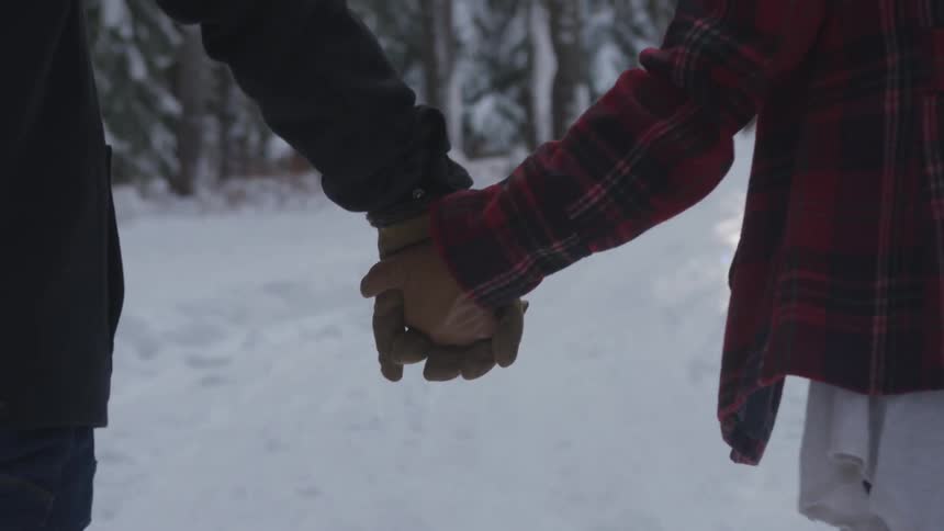 Two people walk hand in hand towards the forest thru the snow