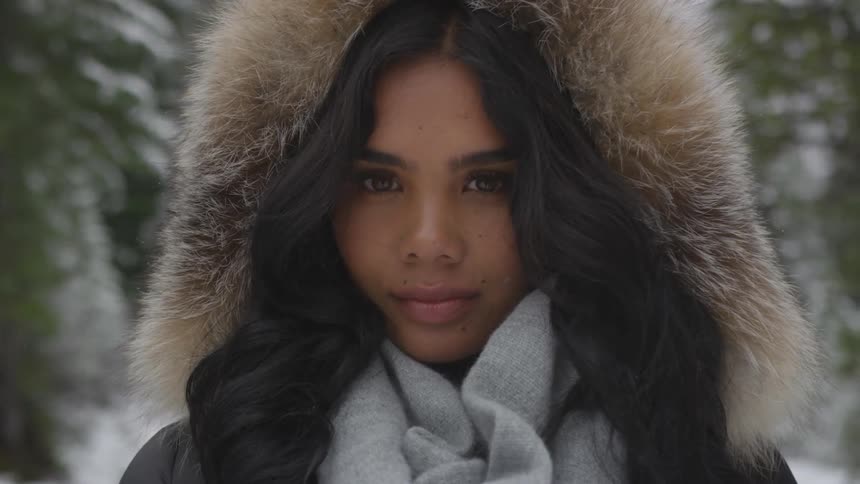 A black woman in a winter coat standing outdoors on a snowy day looking at the camera
