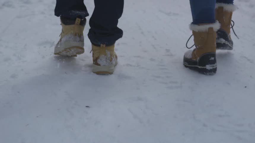 Two people wear snow boots while walking in snow