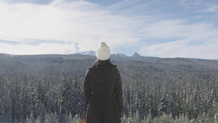 A woman in a coat and winter hat stands in a forest