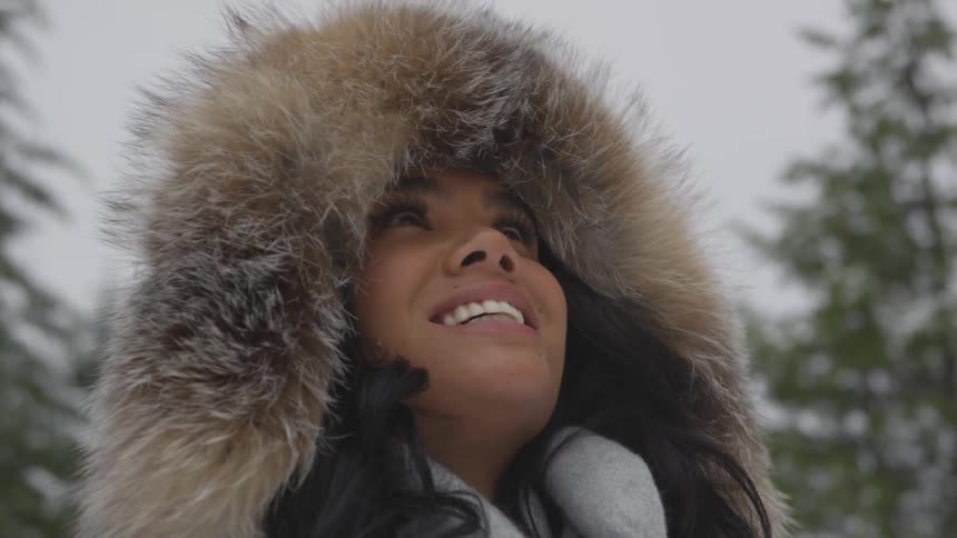 A woman smiles while wearing a fur lined coat in a snowy forest