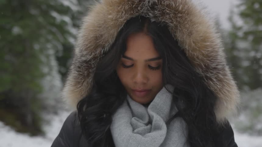 Woman wearing a fur trimmed hood stands in the snowy forest
