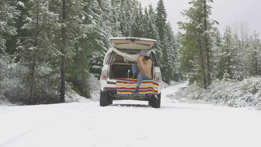 Woman sits in the back of a vehicle sipping a hot beverage in the winter