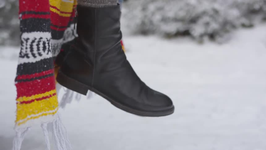 Woman's black leather ankle boots on feet swinging in air above snow