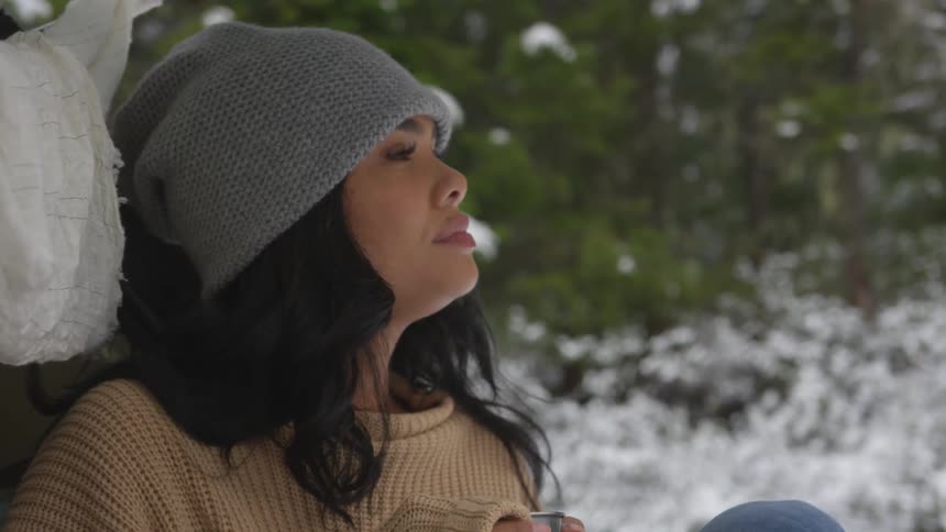 Woman sits outdoors drinking from a mug in winter