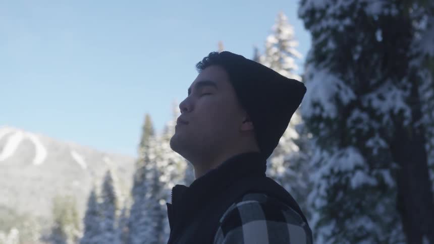 A person stands in a snowy forest with their eyes closed